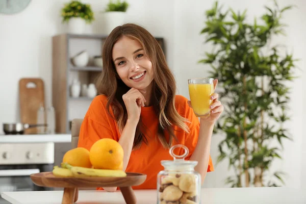 Beautiful young woman drinking orange juice in kitchen — Stock Photo, Image