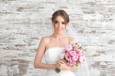 Ahşap arka planda düğün buketi olan güzel genç gelinin portresi.