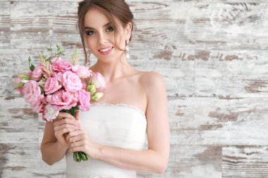 Ahşap arka planda düğün buketi olan güzel genç gelinin portresi.