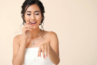 Güzel genç Asyalı gelin açık renk arka planda alyansını gösteriyor.