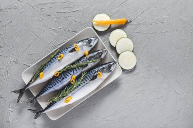 Gri arka planda çiğ uskumru balığı ve sebzeli tabak.