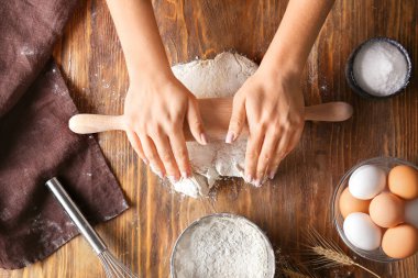 Kadın ahşap arka planda hamur çıkarıyor.