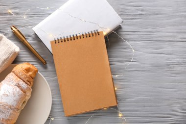 Gri ahşap arka planda kalem, kruvasan ve çelenk bulunan defterler.