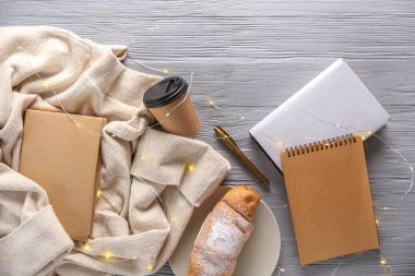 Üzerinde kahve, kruvasan, süveter ve çelenk olan defterler.