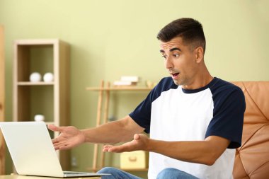 Evde dizüstü bilgisayarla şok olmuş genç bir adam.