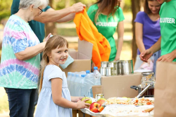 Little poor girl receiving food from volunteers outdoors