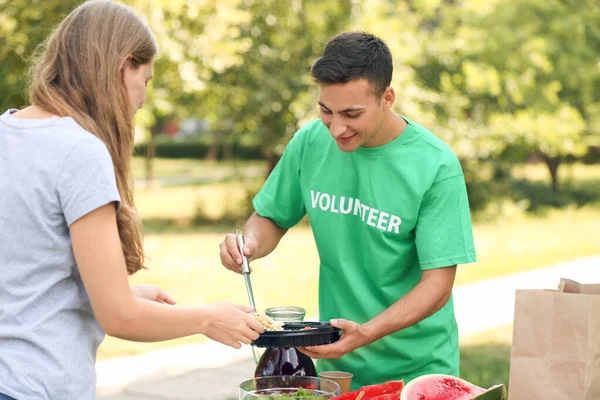 Joven voluntario dando comida para la pobre mujer al aire libre — Foto de Stock
