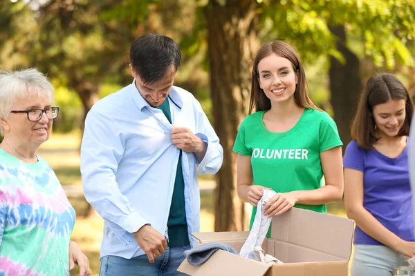 Young volunteer giving new clothes for poor people outdoors — Stock Photo, Image
