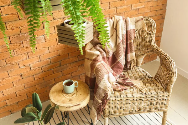 Плетеное кресло, стол и комнатные растения возле кирпичной стены — стоковое фото