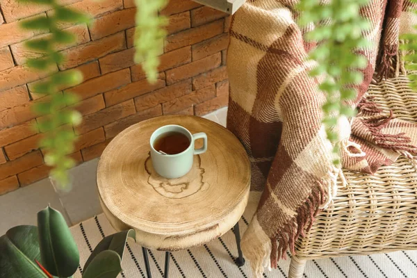 Comfortable wicker armchair and table with cup of tea near brick wall — Stock Photo, Image