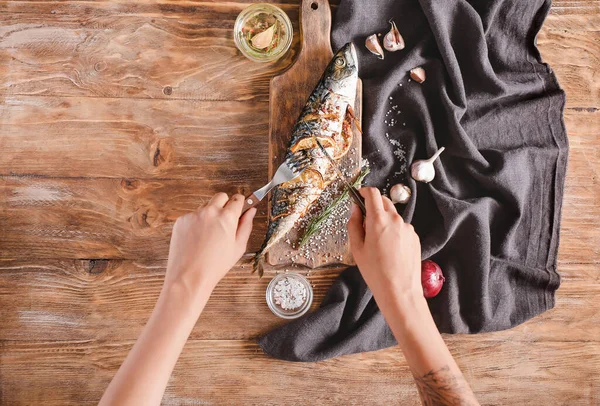 Mujer comiendo sabroso pescado de caballa en la mesa de madera, vista superior —  Fotos de Stock