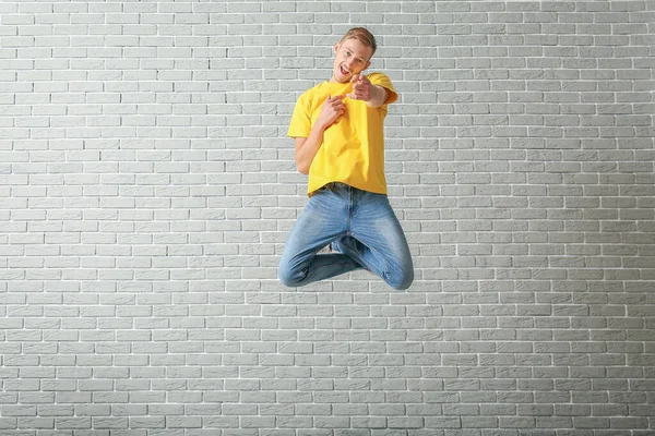 Jumping man in stylish t-shirt on brick background — ストック写真