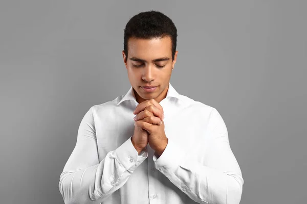 Young African-American man praying on grey background — Stock Photo, Image
