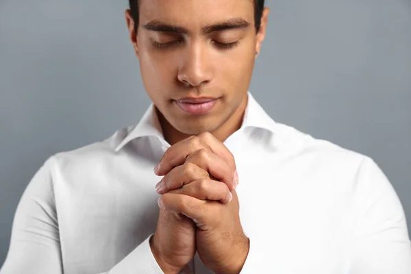 Young African-American man praying on grey background — Stock Photo, Image