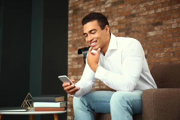 Young African-American man with mobile phone at home — Stock Photo, Image