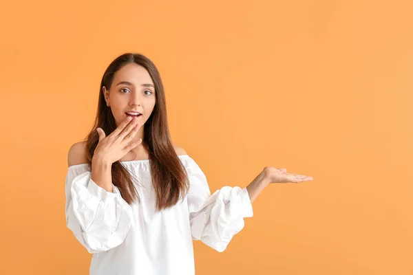 Surprised young woman showing something on color background — Stock Photo, Image
