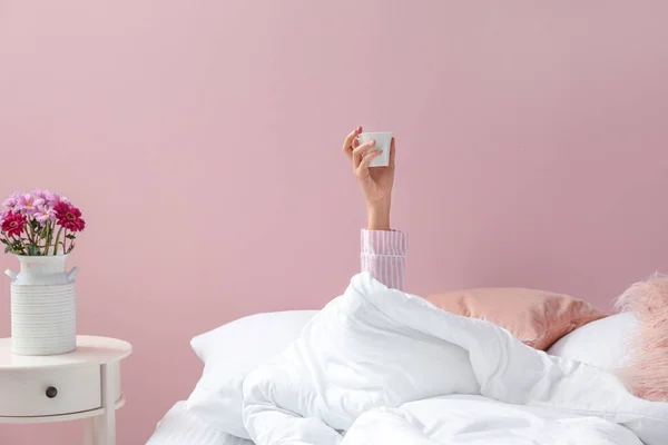 Giovane donna con tazza di caffè sdraiata a letto — Foto Stock