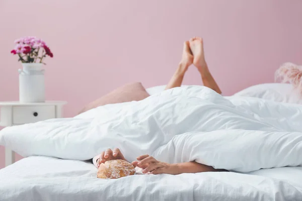 Young woman reaching hands for tasty bun while lying in bed — Stock Photo, Image