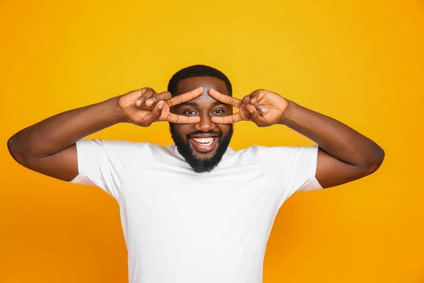 Handsome African-American man showing victory gesture on color background — Stock Photo, Image