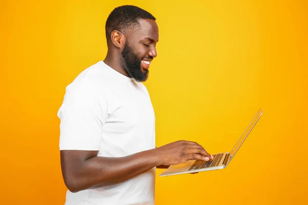 Handsome African-American man with laptop on color background — Stock Photo, Image