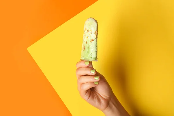 Female hand with tasty pistachio ice cream on color background — Stock Photo, Image