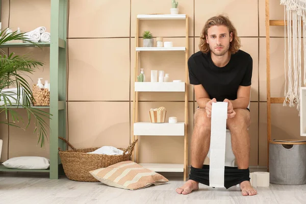 Young man sitting on toilet bowl at home — Stock Photo, Image