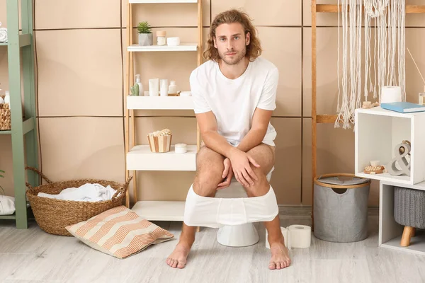 Young man sitting on toilet bowl at home — Stock Photo, Image