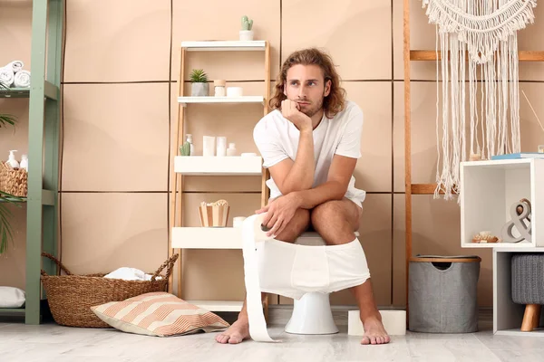 Young man sitting on toilet bowl at home — Stock Photo, Image