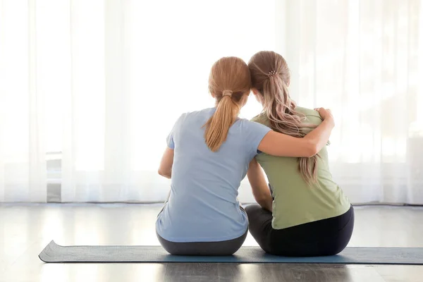 Mother and daughter hugging while sitting on yoga mat at home — Stock Photo, Image