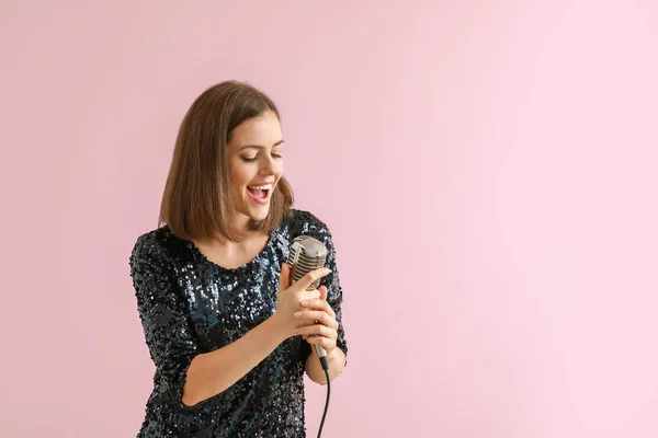 Mooie jonge zangeres met microfoon op kleur achtergrond — Stockfoto