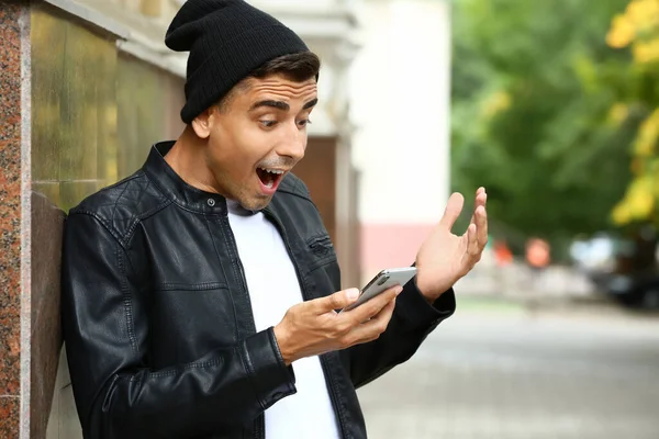 Surprised young man with mobile phone outdoors — Stock Photo, Image