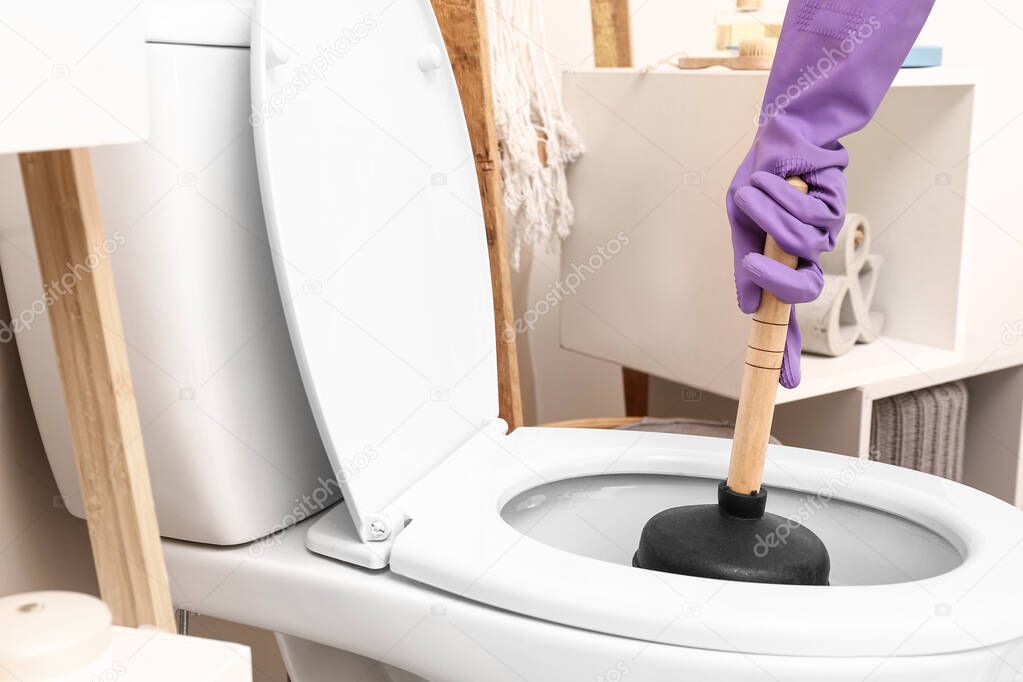 Man using plunger to unclog a toilet bowl