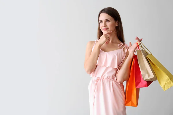 Jovem mulher pensativa com sacos de compras no fundo claro — Fotografia de Stock