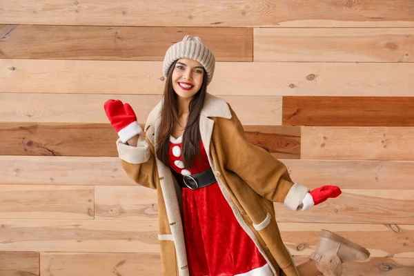 Beautiful young woman in Santa Claus costume against wooden wall — Stock Photo, Image