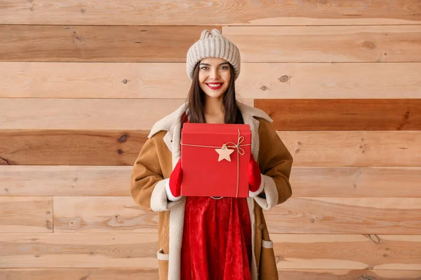 Hermosa mujer joven en traje de Santa Claus y con regalo contra la pared de madera —  Fotos de Stock