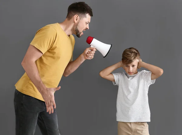 Little boy ignoring his angry father with megaphone against grey background — Stock Photo, Image