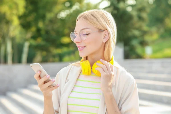 Hermosa mujer joven con auriculares y teléfono móvil al aire libre — Foto de Stock