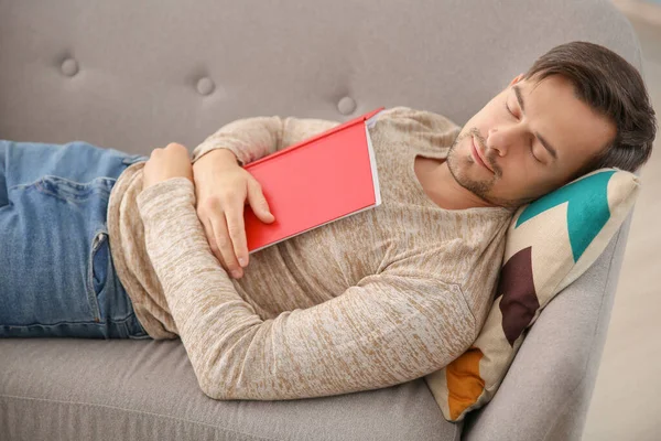 Красивый мужчина с книгой спит на диване дома — стоковое фото