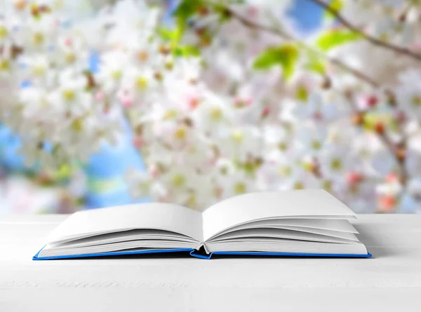 Livre ouvert avec des pages blanches sur la table sous un arbre en fleurs à l'extérieur — Photo