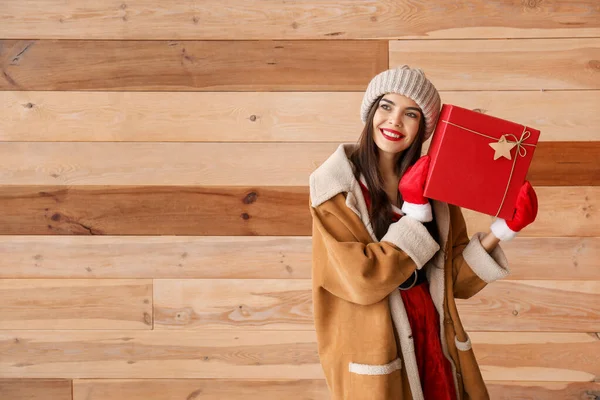 Όμορφη νεαρή γυναίκα με χριστουγεννιάτικο δώρο ενάντια σε ξύλινο τοίχο — Φωτογραφία Αρχείου