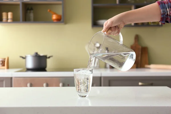 Frau gießt frisches Wasser aus Krug in Glas auf Tisch — Stockfoto