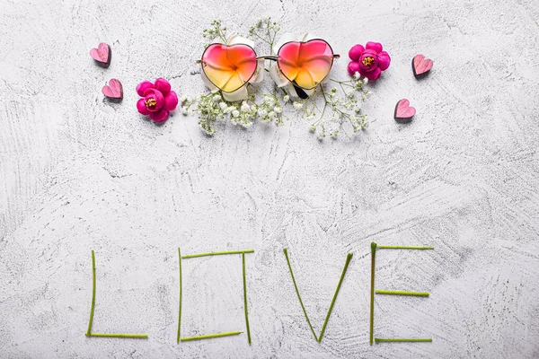 Composition with word LOVE, flowers and sunglasses on light background