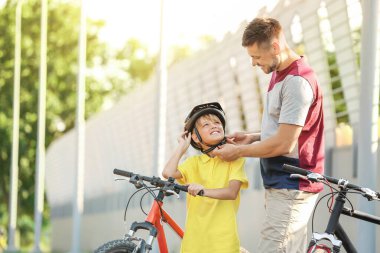 Baba açık havada bisiklet kask koymak için oğlu yardım