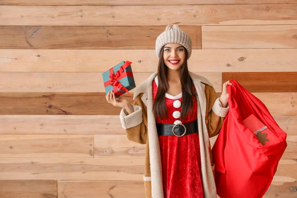 Hermosa mujer joven en traje de Santa Claus y con bolsa contra pared de madera —  Fotos de Stock