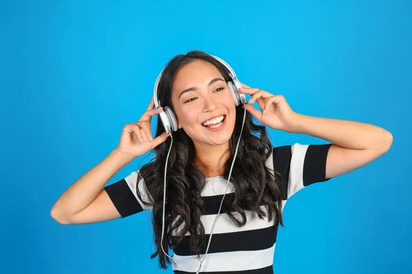 Hermosa mujer asiática escuchando música sobre fondo de color — Foto de Stock
