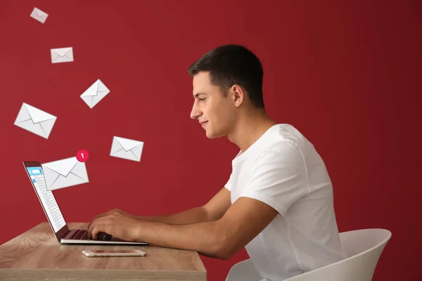 Young man with laptop checking an email while sitting at table against color background — Stock Photo, Image