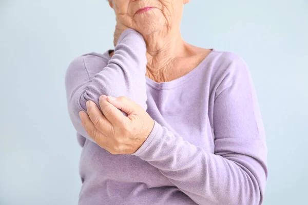 Senior woman suffering from pain in elbow against light background, closeup — Stock Photo, Image