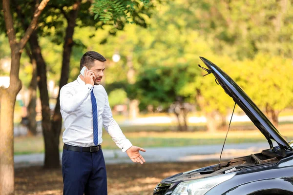 Бізнесмен розмовляє по телефону біля розбитого автомобіля на відкритому повітрі — стокове фото