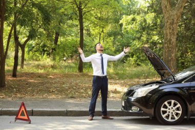 Stresli iş adamı, kırık bir arabanın yanında.