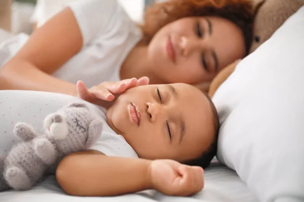 Young African-American woman and her sleeping baby on bed — Stock Photo, Image